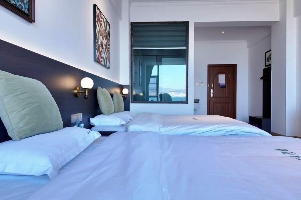 A hotel room with two beds, a large window, and a door leading to another room.