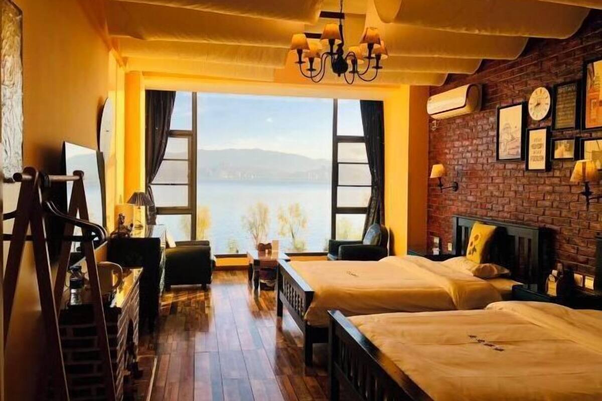 Une chambre avec deux lits, un bureau, une chaise, un lustre et une grande fenêtre donnant sur l’eau.