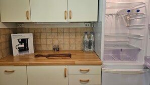 Ett kök med vita skåp, en kaffebryggare, två vattenflaskor och en träskärbräda på bänkskivan.
