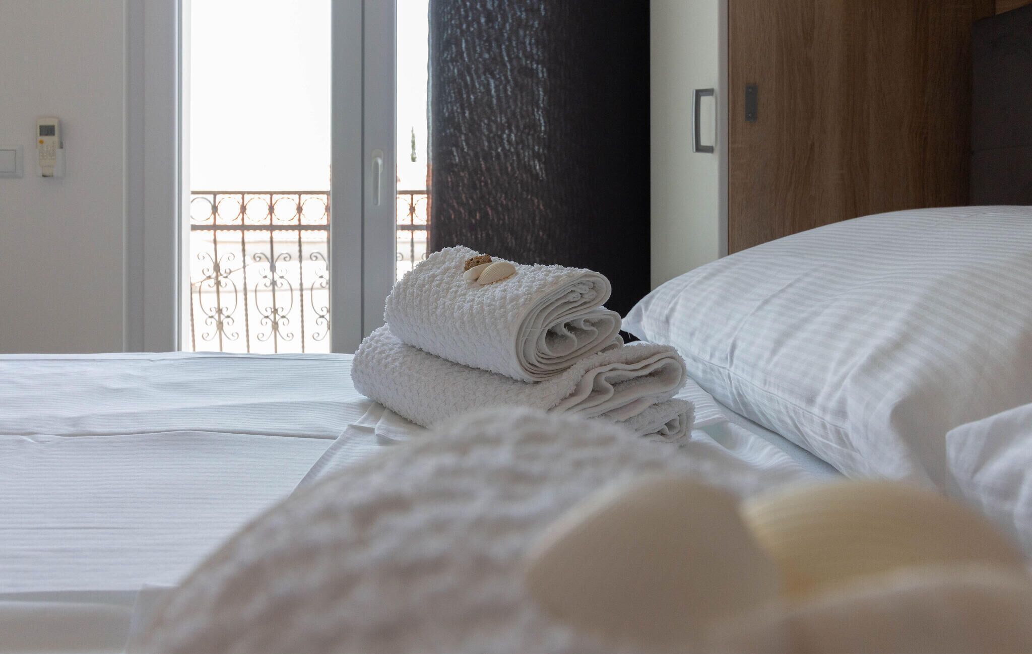 A neatly made bed with white linens and a rolled towel on the side.