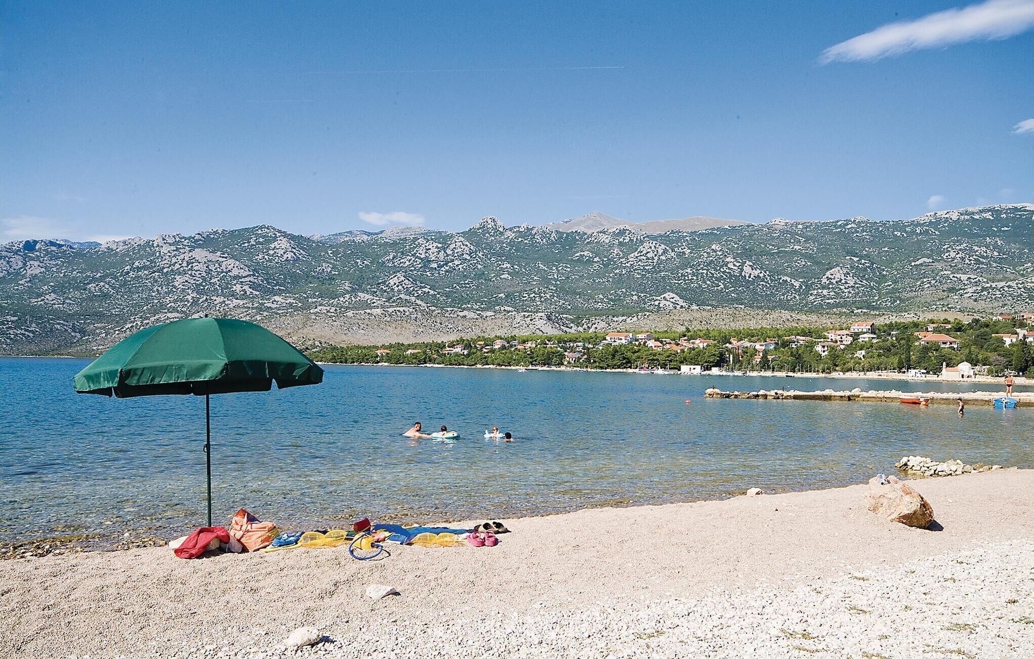 A beach with a green umbrella, people sunbathing, and a mountain backdrop.