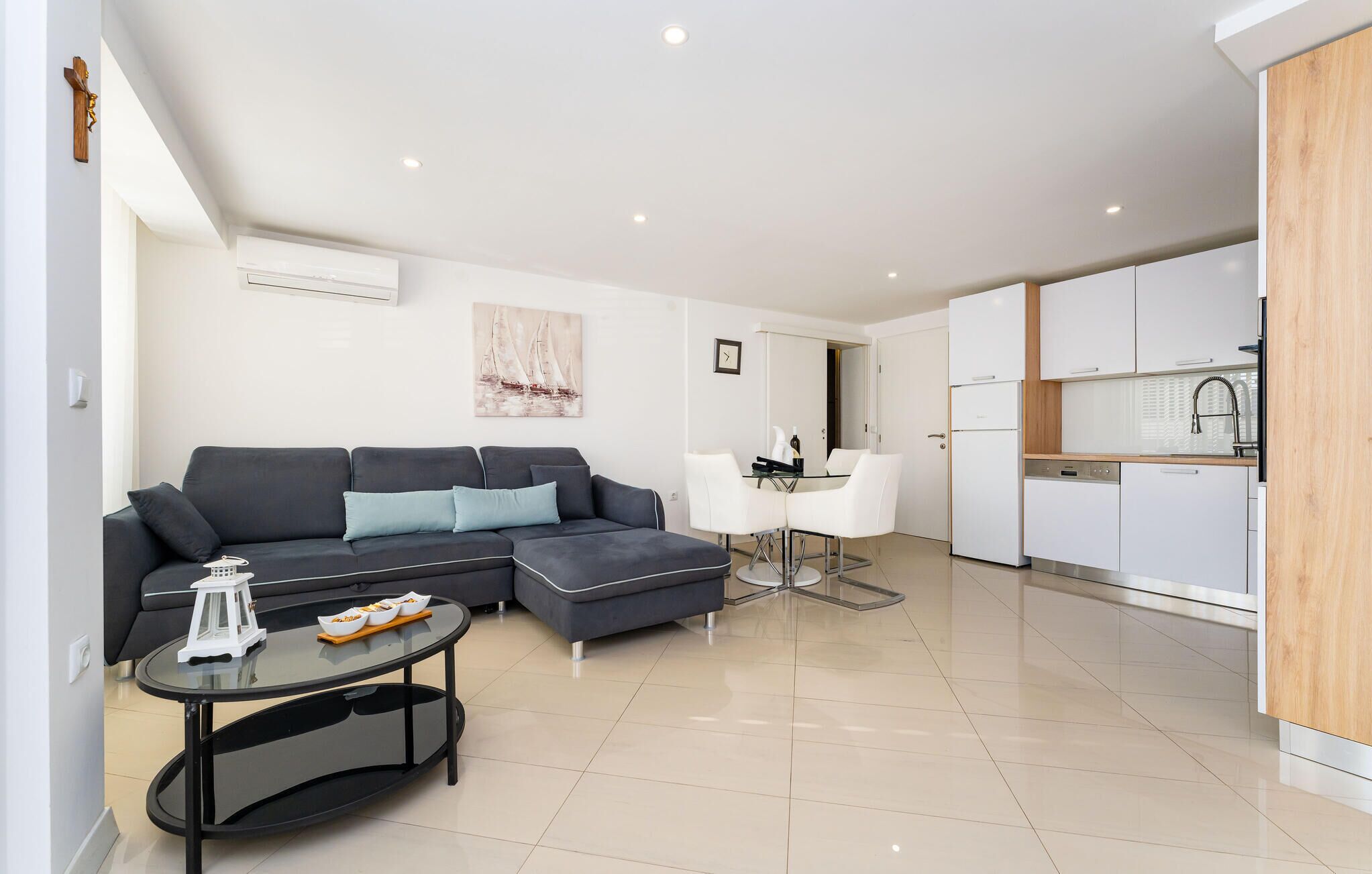 A modern living room with a sectional sofa, a glass coffee table, and a dining area with white chairs.
