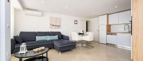 A modern living room with a sectional sofa, a glass coffee table, and a dining area with white chairs.