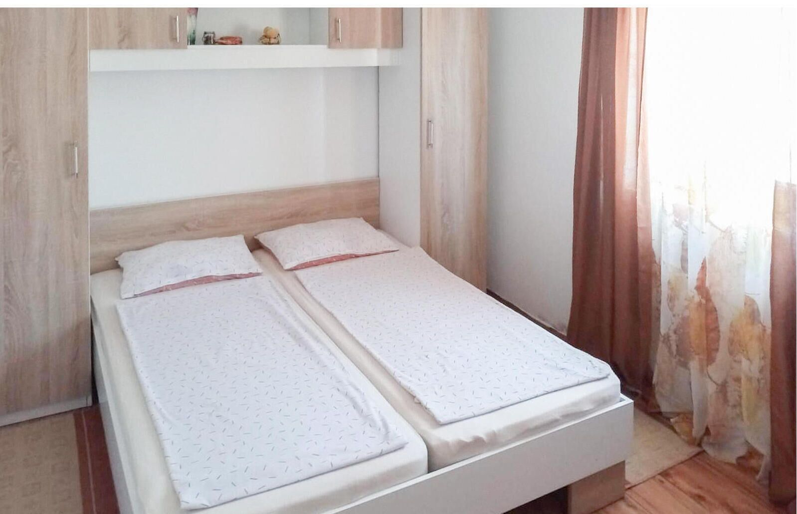 A double bed with a wooden headboard and a white mattress. There is a small shelf above the bed with decorative items.