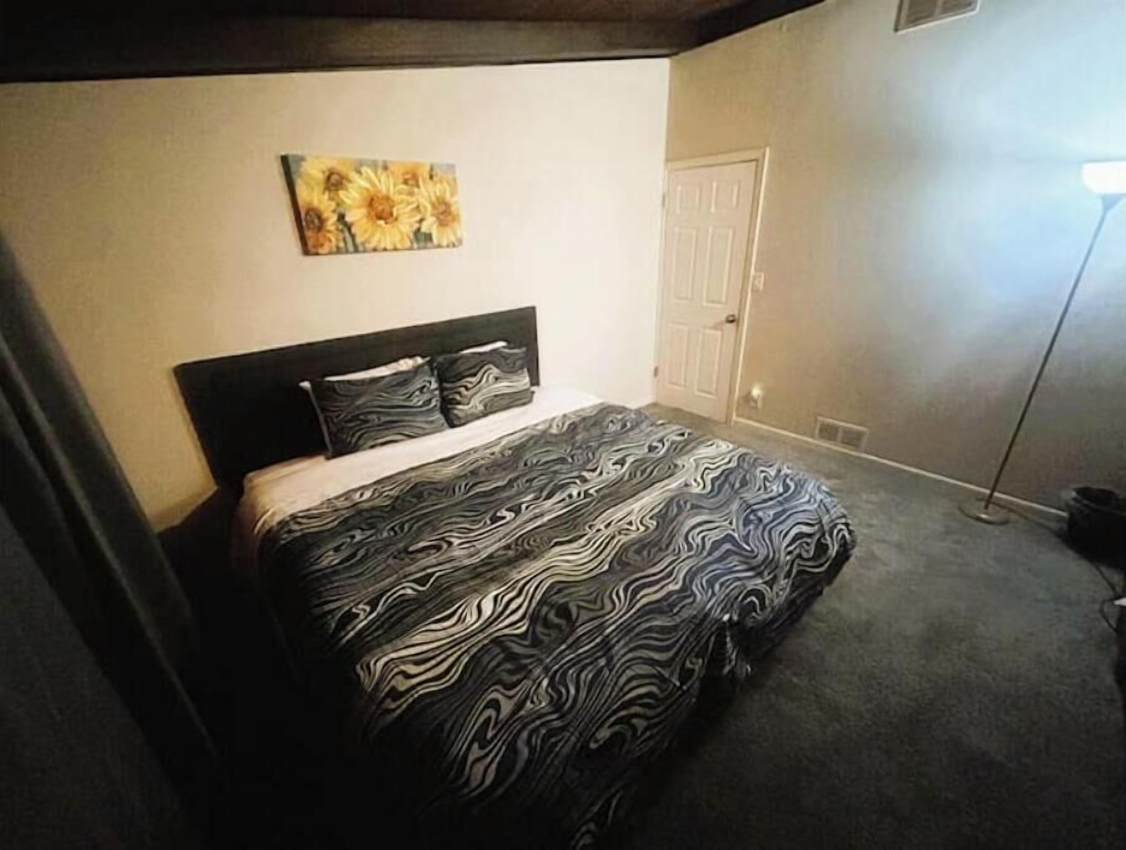 A bedroom with a large bed, a headboard, a painting on the wall, and a door.