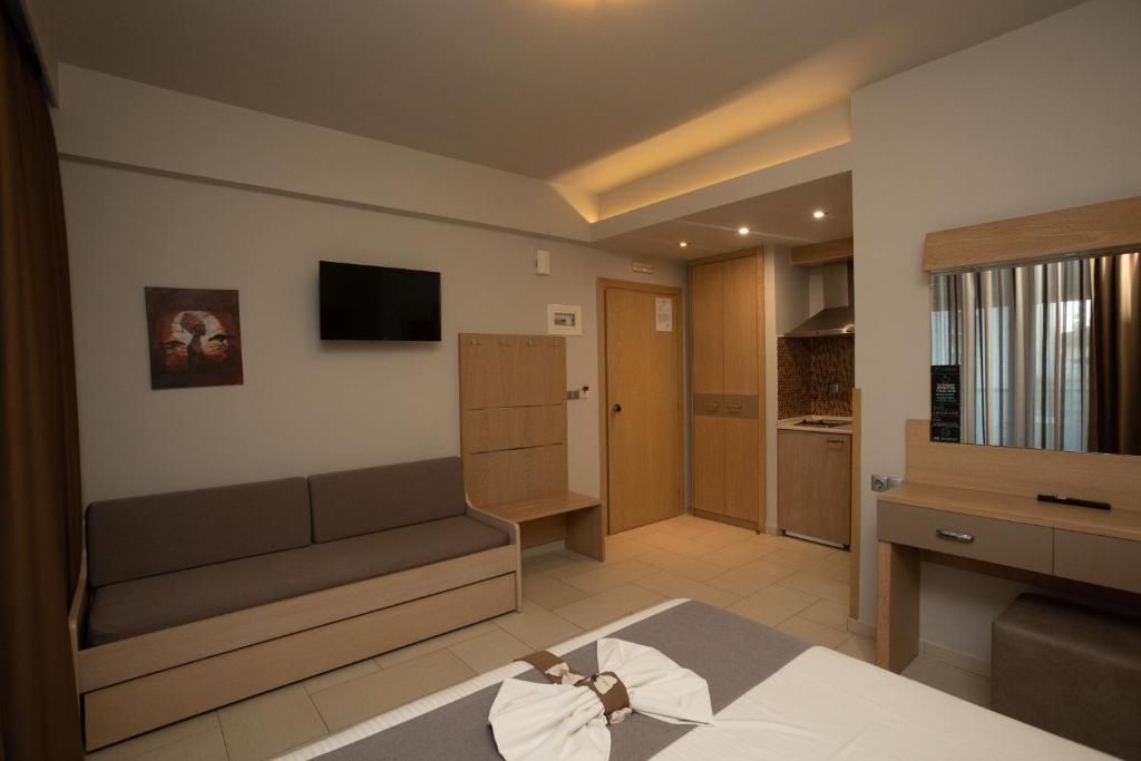 Ein modernes Hotelzimmer mit einer Couch, einem Flachbildfernseher, einer kleinen Küchenzeile und einem Holzkasten.