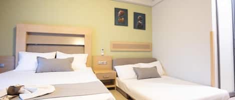 A hotel room with two single beds, a bedside table with a lamp, and a wall-mounted TV.