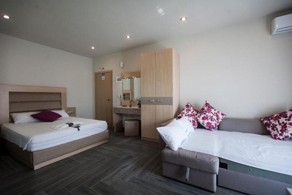 A modern hotel room with a bed, a sofa, a desk, and a wardrobe.