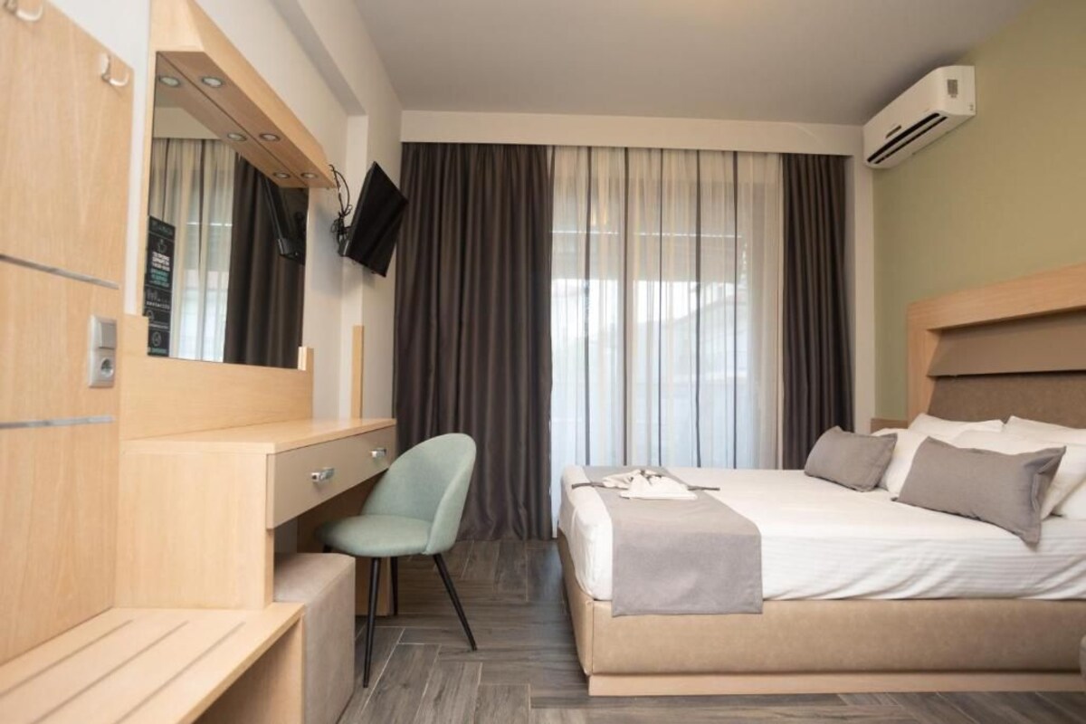 A hotel room with a bed, a desk with a chair, a TV mounted on the wall, and an air conditioning unit.
