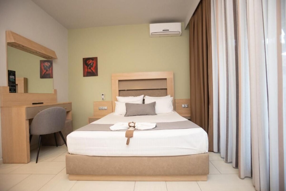 A hotel room with a large bed, a desk, a chair, a mirror, and a window with curtains.
