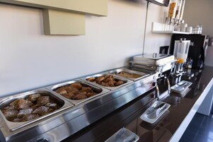 Una barra de buffet con diversos alimentos en recipientes metálicos.