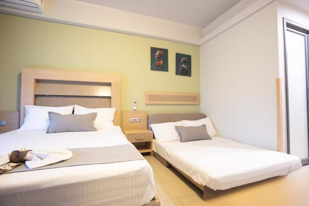 Una habitación de hotel con dos camas individuales, una mesita de noche con lámpara y una televisión instalada en la pared.