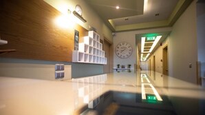 Un moderno vestíbulo de hotel con un mostrador de recepción de madera, un gran reloj de pared y un largo pasillo con piso reflectante.