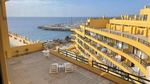 Un edificio amarillo con balcones que dan a un muelle rocoso y al mar.