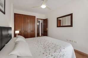 A bedroom with a bed, a ceiling fan, wooden wardrobe, and a mirror on the wall.