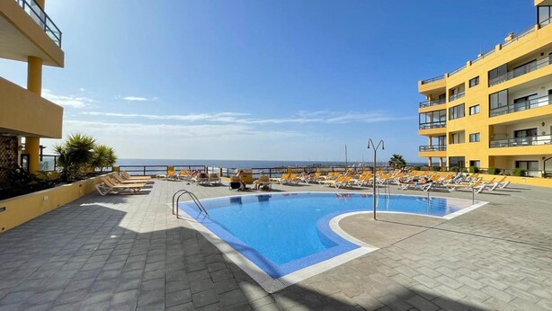 Una piscina en la azotea con tumbonas y vista al mar.