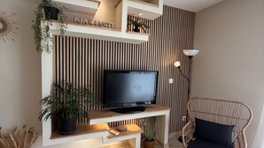 Una sala de estar moderna con un televisor sobre un soporte de madera, una silla de mimbre y plantas decorativas.
