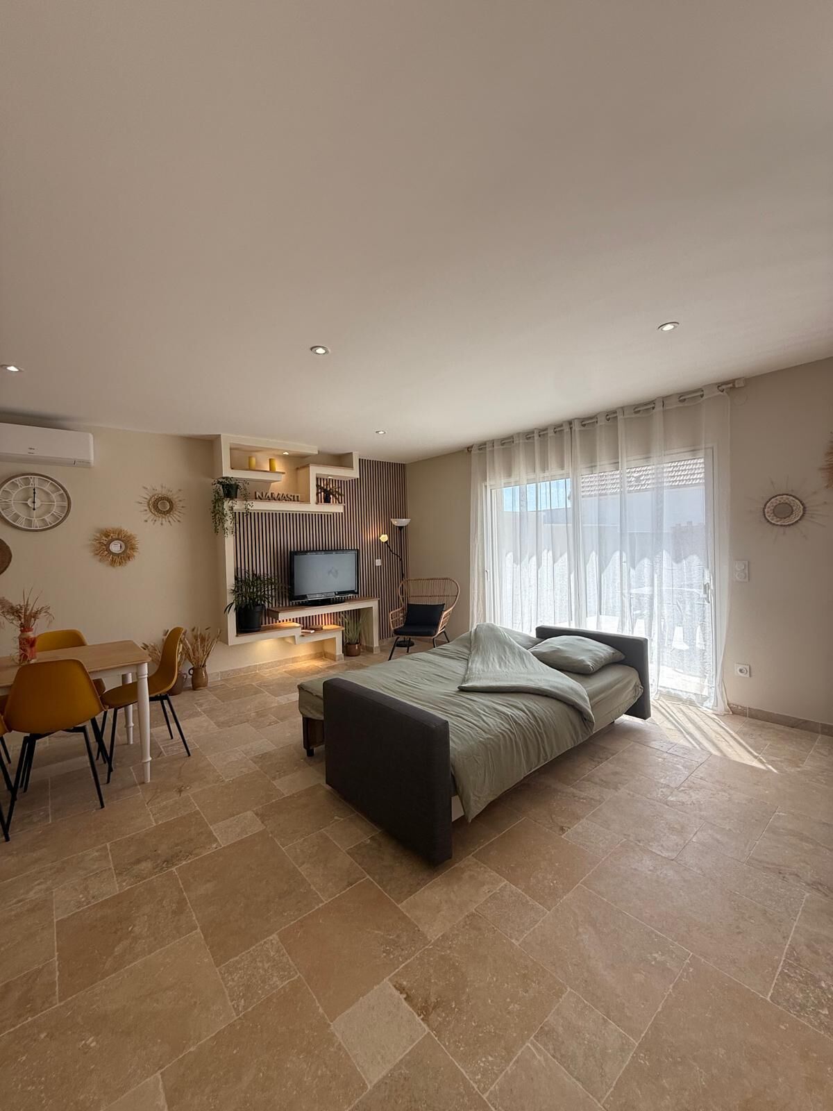 Ein modernes Schlafzimmer mit einem Bett, einem Fernseher, einer Essecke mit Stühlen und einem großen Fenster mit Vorhängen.