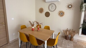 Un comedor con mesa de madera y sillas amarillas, rodeado de adornos en la pared y plantas en macetas.