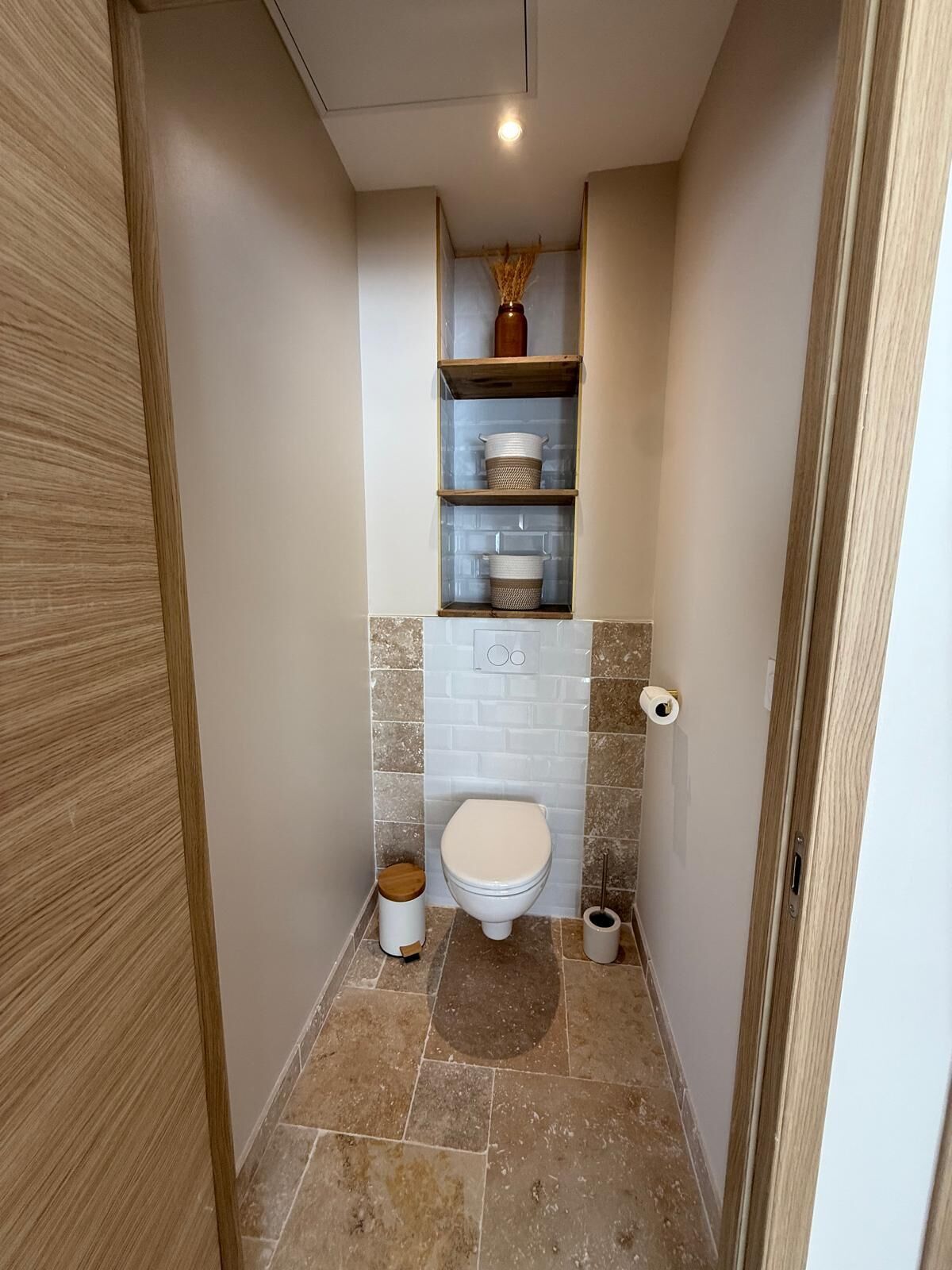 A small, narrow bathroom with a toilet, a shelf above the toilet, and a trash bin.