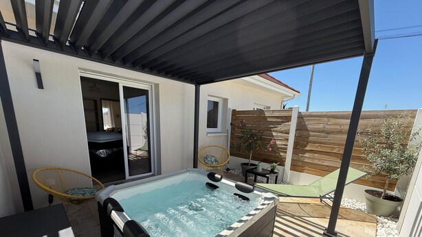 Un jacuzzi, un porche techado, una silla, una mesa y una planta en maceta.