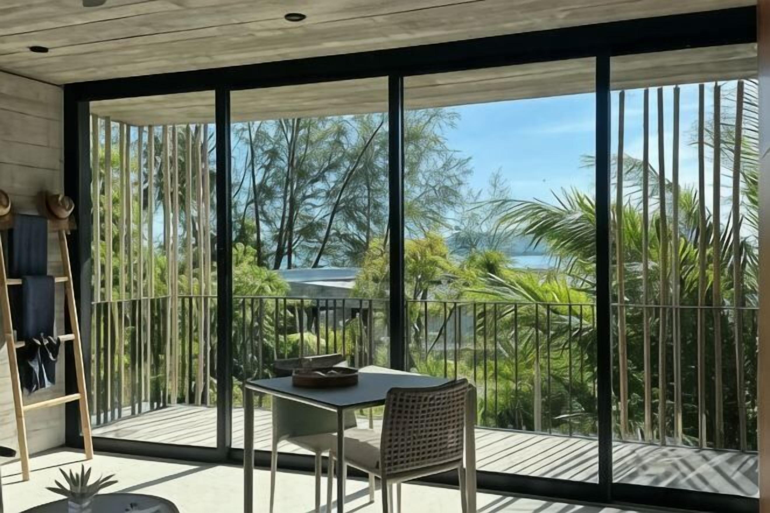 Varanda com mesa, cadeiras, uma escada e vista para o mar e vegetação.