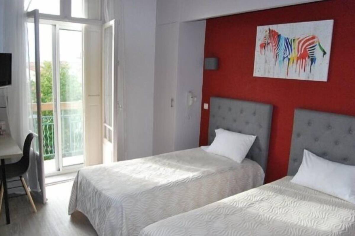 Habitación de hotel con dos camas, una pared de acento roja, un cuadro y un balcón con vistas.