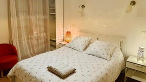 Ein ordentlich eingerichtetes Schlafzimmer mit einem Bett, einem roten Sessel, einem Nachttisch mit Lampe und einer Wandleuchte.