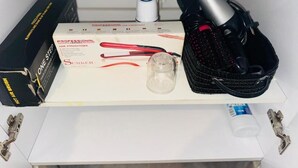 Ein Badezimmerschrank mit einem Glätteisen, einer Bürste, einer Shampoo-Flasche und einer Packung Haarfärbemittel.