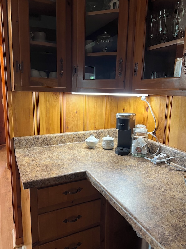 Una cocina con armarios de madera, encimera de granito, cafetera y un tarro de utensilios.