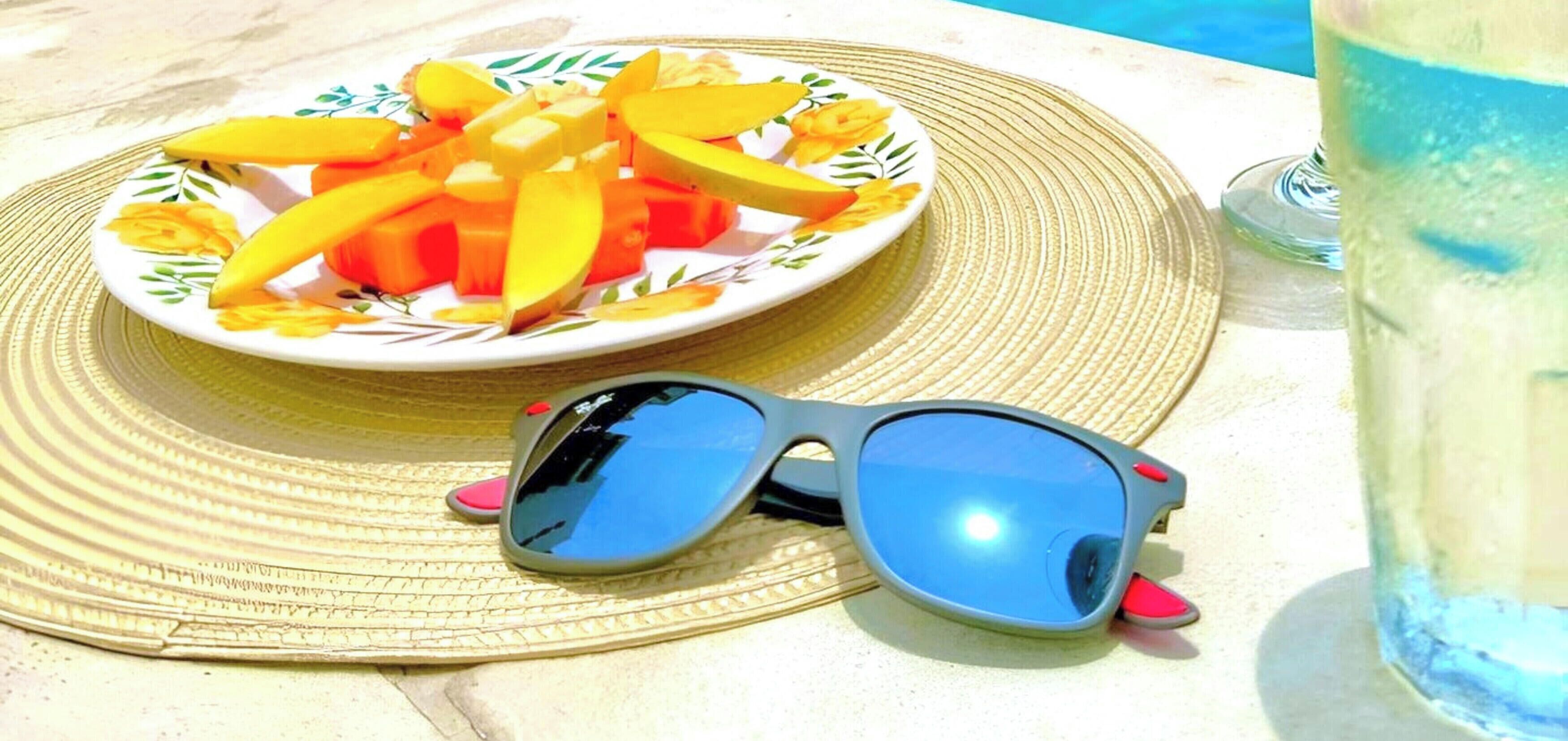 Une assiette de fruits, des lunettes de soleil et un verre d’eau sur une table.