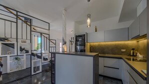 A modern kitchen with a central island, built-in appliances, and a staircase with glass railings.