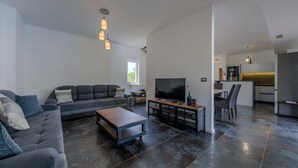 A modern living room with a sofa, coffee table, TV, and a kitchen area with a dining table and chairs.