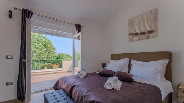 A bedroom with a large bed, a bench, and a view of the outdoors.
