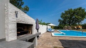 A stone exterior wall with a built-in fireplace, a swimming pool, and a children's play area.