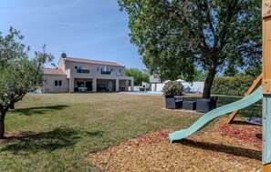 Ein modernes, zweistöckiges Haus mit Swimmingpool, einer Terrasse und Gartenmöbeln sowie einem Kinderspielbereich mit Rutsche.