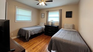 A bedroom with two single beds, a ceiling fan, a dresser, and a television. - The Shaded Retreat (Louisville)