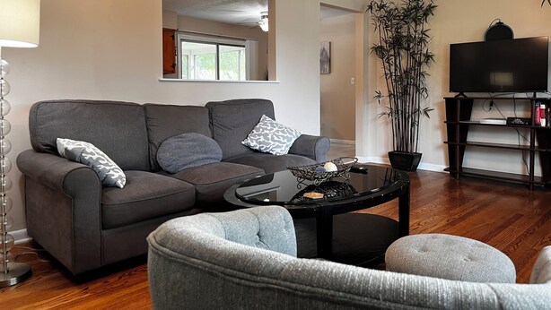 A modern living room with a grey sofa, a round coffee table, and a television on a wooden stand. - The Shaded Retreat (Louisville)