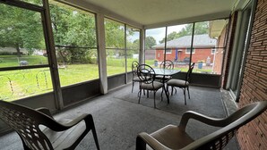 A covered patio with a table and chairs, large windows, and a brick wall. - The Shaded Retreat (Louisville)