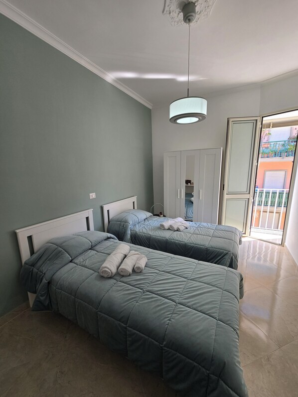 A bedroom with two beds, a ceiling light, a wardrobe, and a view of the outside balcony.