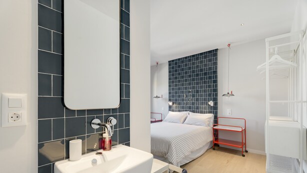 Ein modernes Badezimmer mit einem weißen Waschbecken, einem Spiegel und dunkelblauen Fliesenwänden.