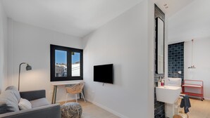 Ein modernes Wohnzimmer mit einer Couch, einem Fernseher, einem Schreibtisch und einem Sessel.