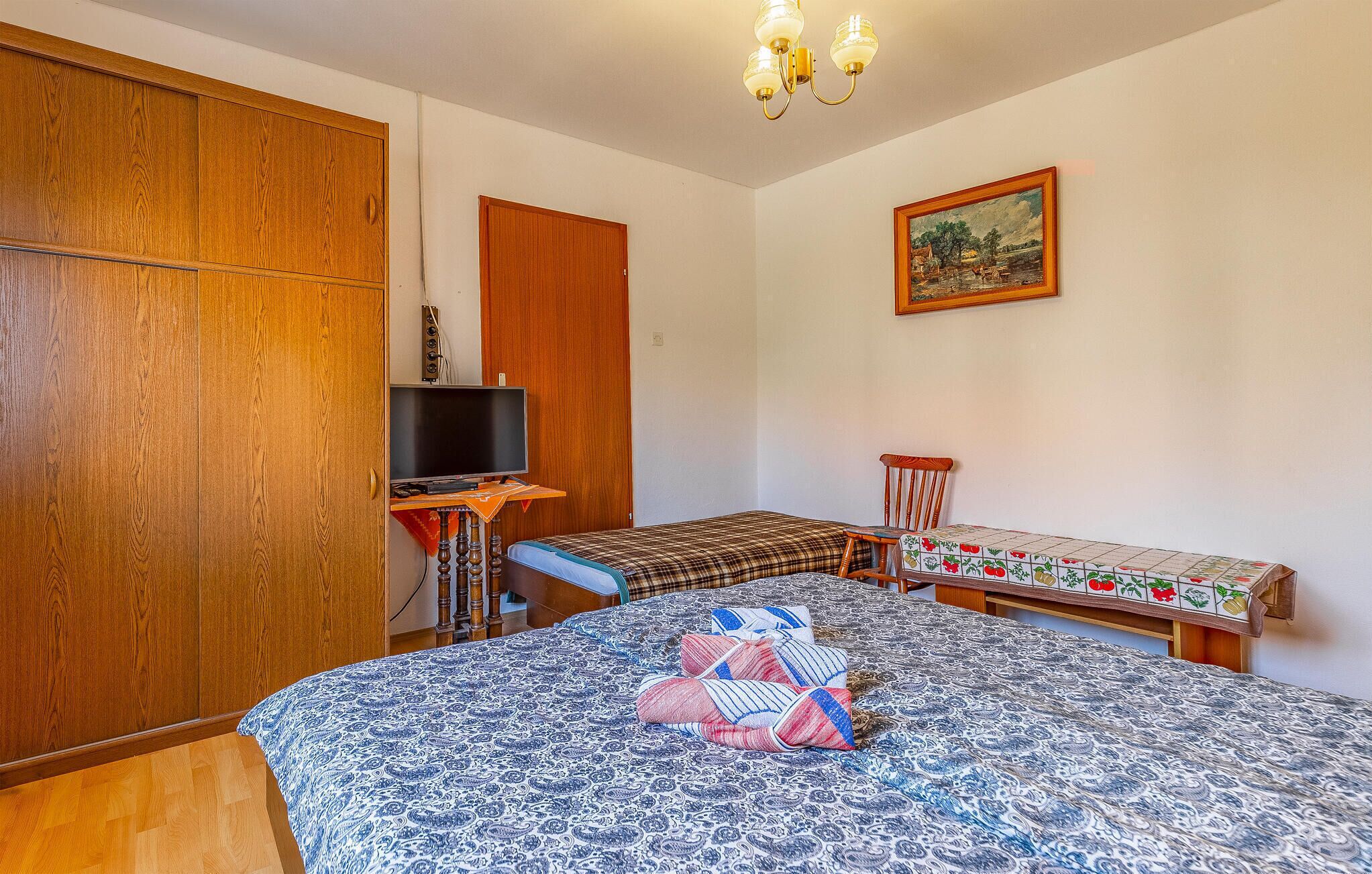 Ein Schlafzimmer mit einem Bett, einem Fernseher auf einem Schrank, einem Holzschrank, einem Bild an der Wand und einem kleinen Tisch mit einem Stuhl.