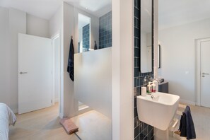 Un baño moderno con un lavamanos blanco, baldosas oscuras y un espejo.