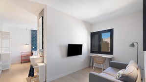 A modern living room with a flat-screen TV, a sofa, a small table, and a window with blinds.