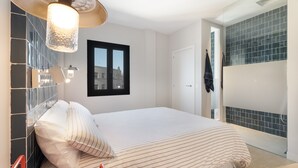 A bedroom with a bed, a hanging light fixture, a window, and a tiled wall.