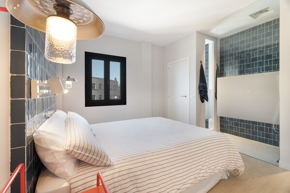 Un dormitorio con cama, lámpara colgante, ventana y pared con azulejos.