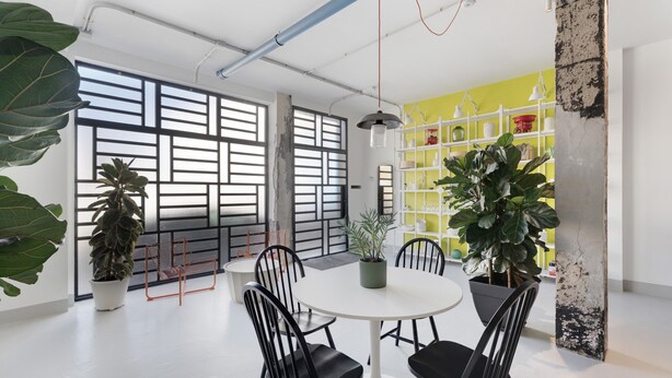 A modern meeting room with a round table, black chairs, potted plants, and a yellow shelving unit.