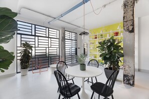 Una sala de reuniones moderna con una mesa redonda, sillas negras, plantas en macetas y un estante amarillo.