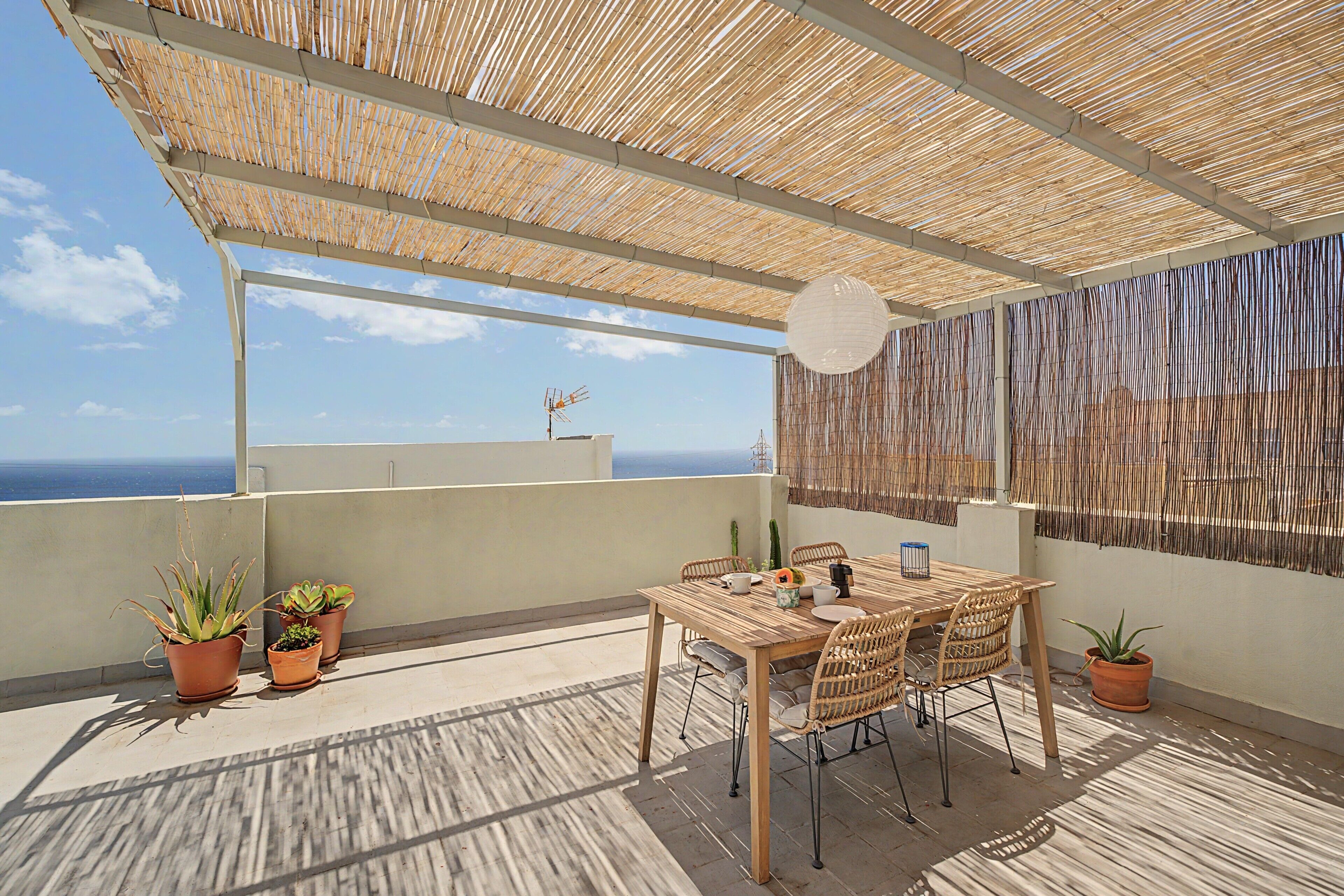 A rooftop terrace with a table and chairs, potted plants, and a view of the sea.